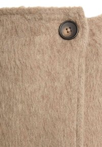 Tant wolachtige stof met een zachte, gestructureerde afwerking en een zwart knoopdetail. De stof heeft een rafelige rand aan één zijde.