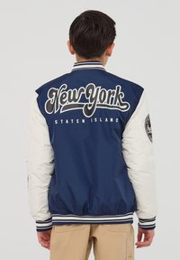 Granatowa i biała kurtka varsity z napisem "New York Staten Island" w wyraźnym druku na plecach, z prążkowanymi mankietami i dołem oraz kontrastującymi rękawami.