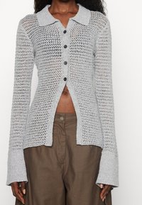 Cardigan in grigio chiaro lavorato a maglia con design a colletto, bottoni sulla parte anteriore e maniche ampie. Motivo a tessitura aperta con una vestibilità leggermente accorciata.