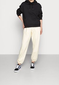 Zwarte oversized hoodie met trektouw, crèmekleurige getailleerde joggingbroek en zwarte sneakers met kleurrijke accenten. Gladde stoftexturen.