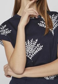 Námořnická modrá bavlněná tričko s krátkými rukávy, zdobené bílými květinovými listovými vzory, hladká textura a kulatý výstřih.