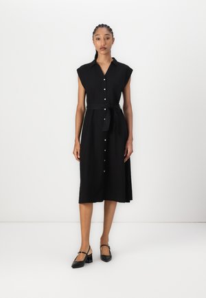 Robe noire boutonnée avec de courtes manches les capes, une ceinture à la taille et une silhouette fluide. Présente des boutons ronds et tombe sous le genou.