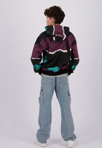 Flerfarget hettegenser i svart, lilla og teal med snøring i hetten; parret med lyseblå cargo-jeans og hvite sneakers.