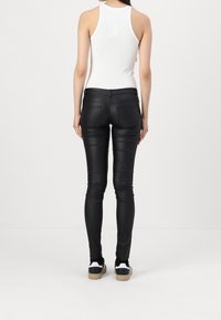 Black faux leather skinny pants with a smooth texture, featuring back pockets and a mid-rise waist, paired with black and white sneakers.