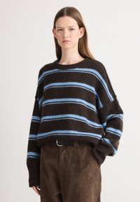 Braun gestreifter Pullover mit blauen Horizontalstreifen, aus einem strukturierten Strickmaterial. Getragen mit braunen Cordhosen und einem schwarzen Gürtel.