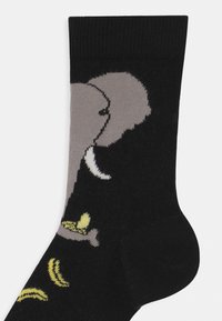 Meias pretas com um gráfico de elefante cinza e bananas amarelas, feitas de material tricotado, com punhos canelados e textura suave.