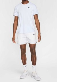 Camisa Nike de manga corta azul claro, pantalones cortos blancos con detalles en los bolsillos, calcetines blancos y zapatos Nike grises. Diseño simple con acentos mínimos.