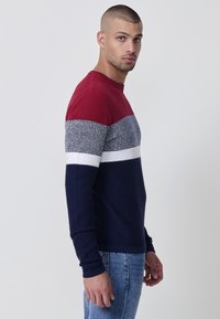 Maglione da uomo in maglia con design a blocchi di colore, comprendente sezioni rosse, grigie, bianche e blu navy. Tessuto a coste testurizzato con maniche lunghe.