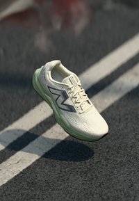 Weißer Sportschuh mit strukturiertem Obermaterial, ausgestattet mit grauen Akzenten und einer hellgrünen Sohle. Einfaches Schnürsystem, entwickelt für das Laufen oder Training.