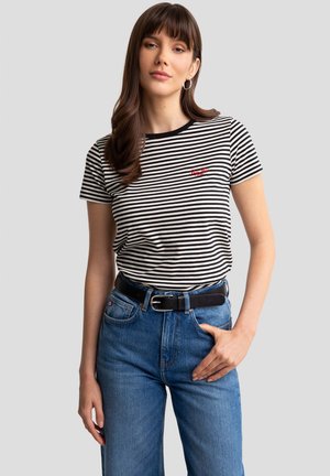 Czarny i biały t-shirt w paski z krótkimi rękawami, okrągłym dekoltem, czerwonym haftem na piersi, zestawiony z niebieskimi dżinsami o wysokim stanie i czarnym paskiem.
