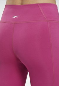 Leggings taille haute fuchsia en tissu extensible avec des coutures plates et un petit logo imprimé à la taille.