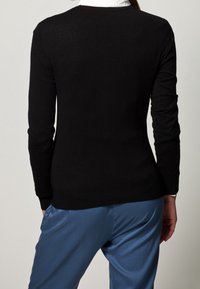 Svart långärmad tröja med en figursydd design, jämn textur och rundad halsringning, matchad med blå löst sittande byxor.