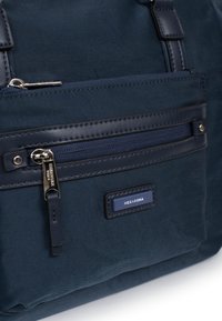 Borsa in nylon blu navy con rifiniture in pelle, dotata di tasca frontale con zip, vista ravvicinata del marchio e superficie liscia.