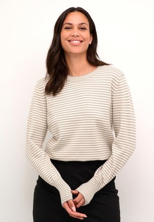 Pull léger à rayures crème et taupe, avec des manches longues, un col rond et des ouvertures pour les pouces aux poignets, associé à une jupe noire.