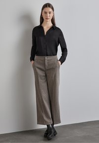Black button-up shirt with long sleeves paired with wide-leg, check-patterned brown trousers. Black chunky heeled ankle boots complete the outfit.