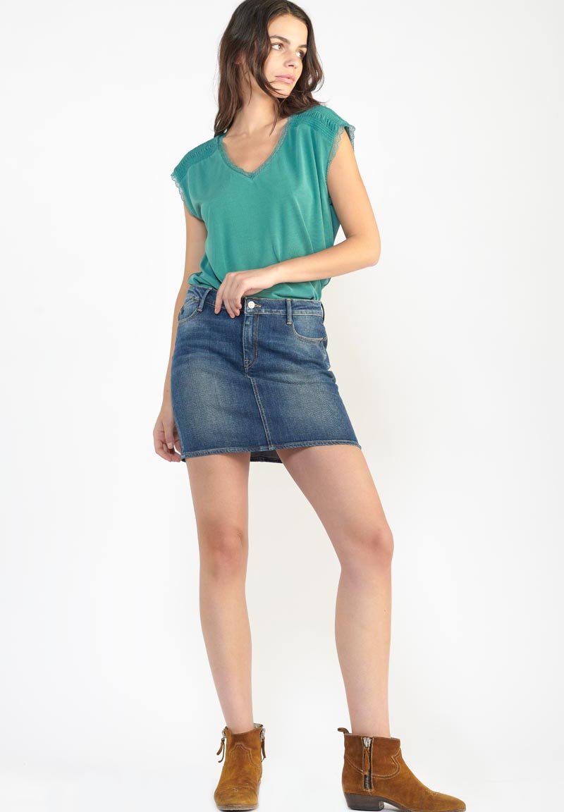 Top teal de decote em v com mangas rendadas, combinado com uma saia mini de denim e botas de tornozelo castanhas. O tecido parece suave com um corte descontraído.