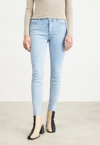 Jeans de corte slim de color azul claro, con una textura suave, que presentan un diseño clásico de cinco bolsillos y una cintura de altura media. Llevados con botas de tacón bloque bicolor.