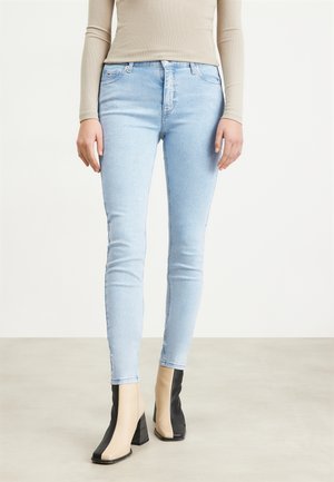 Jeans de corte slim de color azul claro, con una textura suave, que presentan un diseño clásico de cinco bolsillos y una cintura de altura media. Llevados con botas de tacón bloque bicolor.