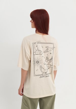 T-shirt oversize beige à manches courtes ; affiche des illustrations en ligne noire d'éléments célestes et d'oiseaux au dos ; matière douce en coton.