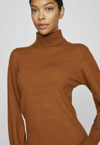 Maglione a collo alto marrone a coste con maniche lunghe. La texture morbida, il design aderente e il collo alto creano una silhouette semplice e classica.