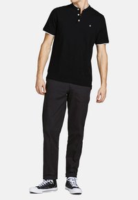 Sort polo skjorte med en tre-knaps placket, hvide accenter på kraven og ærmerne, parret med sorte bukser og sort-hvide sneakers.