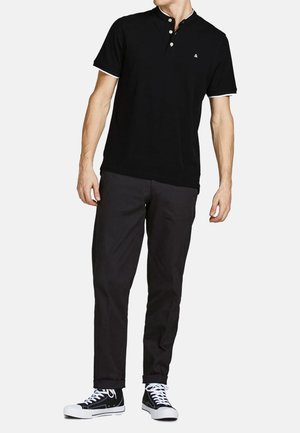 Schwarzes Polohemd mit einem Drei-Knopf-Verschluss, weißen Akzenten am Kragen und den Ärmeln, kombiniert mit schwarzen Hosen und schwarz-weißen Sneakers.