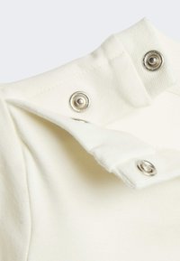 Tela de algodón blanca con cierres automáticos plateados y un borde de cuello texturizado, mostrando una superficie lisa y un aspecto suave.