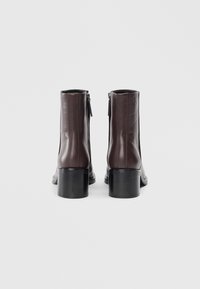 Pair of brown leather ankle boots with block heels, rear zippers, and embossed logo on the upper back, shown from the back on a plain background.