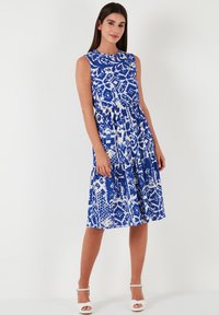 Blue and white patterned sleeveless dress with a round neckline, gathered waist, and flowing skirt, featuring a tiered design.