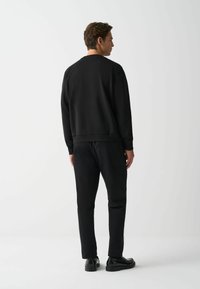 Hanorac negru cu guler rotund, țesătură ușor texturată și manșete ribelate. Asortat cu pantaloni negri slim-fit și pantofi negri strălucitori.