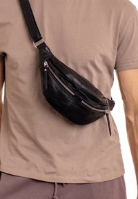 Black leather fanny pack with a curved design, featuring zippered pockets, a textured surface, and an adjustable strap.