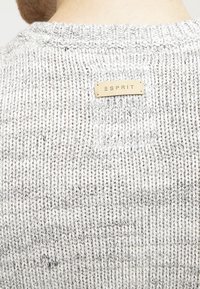 Pull en maille gris clair avec des accents gris plus foncé, présentant un col côtelé et une petite étiquette "ESPRIT" en or à l'arrière.