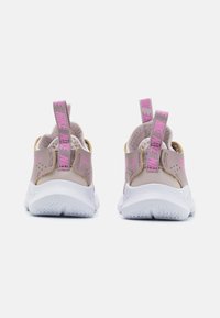 Vaaleanpunaiset urheilukengät valkoisilla pohjilla, joissa on teksturoidut takakumit, kultaiset yksityiskohdat ja vaaleanpunaiset vetolenkit helppoa pukemista varten.