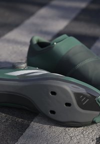 Green athletic shoes feature a textured upper with a smooth heel, rubber sole, and a circular fastening detail on top.