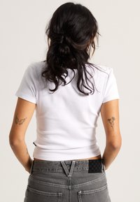 Hvid ribbet crop top med korteærmer, parret med højtaljede grå jeans, der har et ternet lap på baglommen.