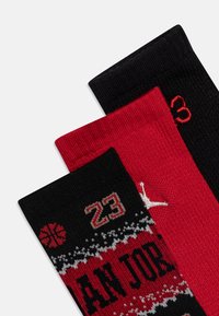 Tre paia di calzini: uno nero con dettagli rossi, uno rosso con motivi neri e bianchi, e uno nero con il numero 23 rosso e un logo.