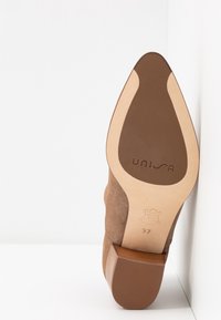 Bruine suède hak schoen met een taps toelopend ontwerp, een stevige blokhak en een gladde leren zool. De binnenzool heeft een reliëf branding en maat.