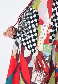 Veelgekleurde oversized jurk met abstracte ontwerpen, dambordpatronen en tekstaccenten. Gemaakt van lichtgewicht, gladde stof.