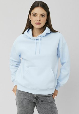 Sweat à capuche bleu clair avec poche avant, capuche à cordon de serrage et poignets côtelés. Tissu doux avec une silhouette décontractée. Jean gris porté en dessous.