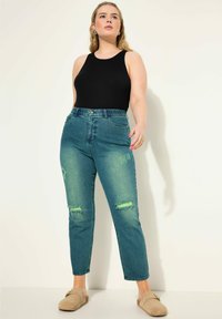 Tmavě modré džíny s vysokým pasem, s otrhanými detaily a rovnými nohavicemi, spárované s černým tílkem a béžovými nazouvacími botami.