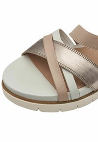 Sandale légère avec une semelle blanche et vert pâle. Brides croisées en beige doux, doré métallique et rose clair, avec un semelle texturée.