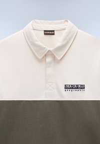 Kortermet polo skjorte i beige og olivengrønn. Har krage, brodert logo og teksturert stoff.