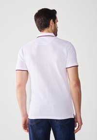 Hvid polo shirt med ribbet krave, der har mørkerøde accenter, korte ærmer og en tætsiddende pasform. Bæres med blå denim jeans.