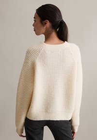 Kremowy sweter dziergany z teksturowanym wzorem, rękawy raglanowe i okrągły dekolt, z prążkowanym dołem i mankietami.
