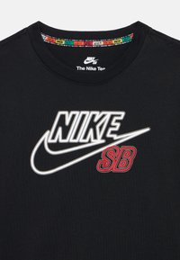 Μαύρο βαμβακερό μπλουζάκι με έντονο λευκό και κόκκινο λογότυπο "NIKE SB" με καμπυλωτό σχέδιο swoosh. Στρογγυλή λαιμόκοψη με διακοσμητική εσωτερική επένδυση.