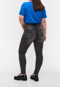 Jeans de tiro alto, de color gris oscuro, con un diseño ajustado, que cuentan con bolsillos traseros y una textura suave. Combinados con una camiseta azul y zapatos negros.