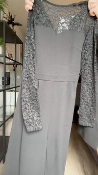 Vestido negro con un corsé ajustado y mangas largas de encaje. El encaje es intrincado, con patrones florales. La tela es suave y texturizada.