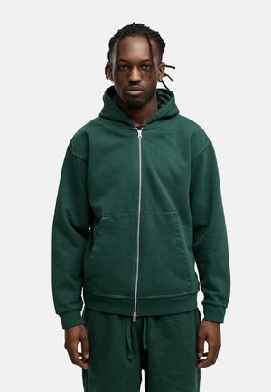 Grüne Kapuzenjacke mit Reißverschluss aus strukturiertem Stoff, ausgestattet mit einer Kängurutasche, einer verstellbaren Kapuze und gerippten Bündchen, kombiniert mit passenden Jogginghosen.