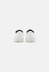 Sneakers in pelle bianca con profilo basso, caratterizzati da un accento in tessuto nero nel tallone e suola in gomma bianca testurizzata.