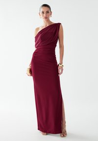 Bordo vienas pleca kleita, izgatavota no mīksta auduma. Tai ir savilkta detaļa jostas vietā un sānu šķēlums, kas veido garāku siluetu.